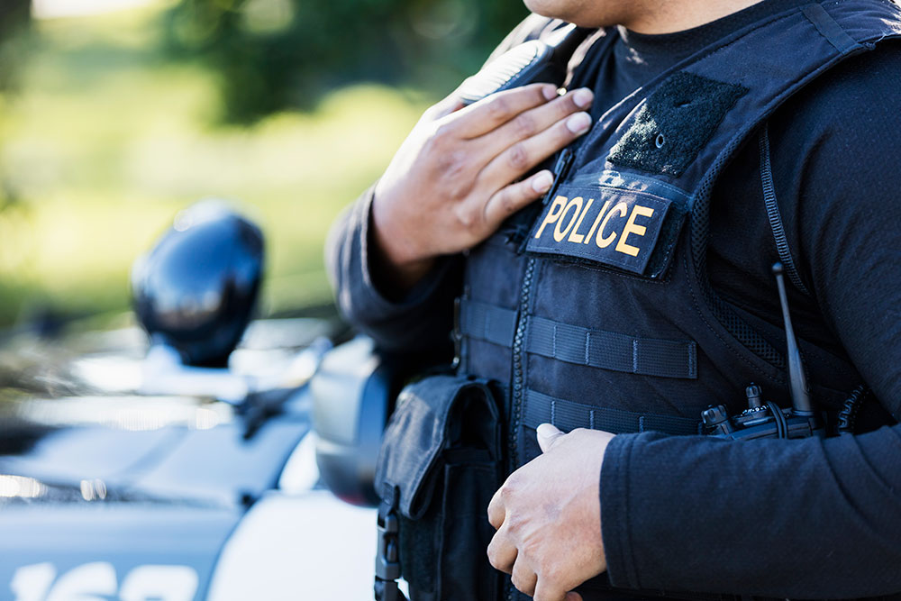 Police officer using a shoulder radio beside a patrol vehicle