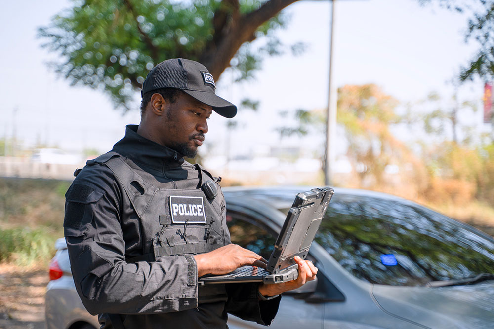 Police officer using a rugged laptop beside a vehicle